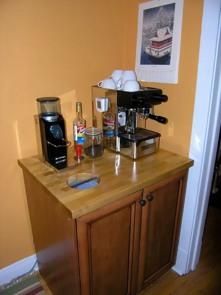 Kleine Kaffeeecke mit Maschine, Mühle und Tassen auf einer Holzkommode